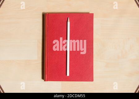 White pencil in a red hardcover on a parquet background and some books in the corners as a frame. Stock Photo