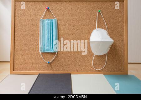 Two masks hanging on a corkboard with some books on the floor on a white background. Stock Photo