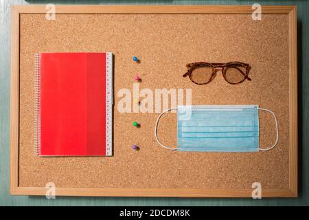 A notebook with alphabetical index separated by a row of colored pins from vintage eyeglasses and a surgical mask with a corkboard in the background. Stock Photo
