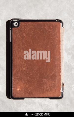 Small photography lens on the back of an old digital tablet with a time-worn leather case. Stock Photo