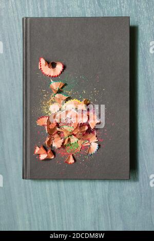 Black hardcover book with pieces of colored pencils on a blue wooden table. Background with space to text. Stock Photo