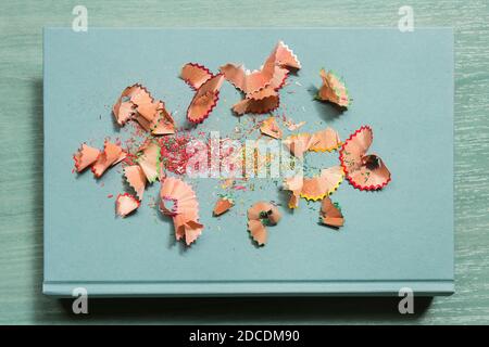 Colored pencil shavings surrounded by scraps of wood on a textured blue book atop a stylish green table. Teamwork concept. Stock Photo