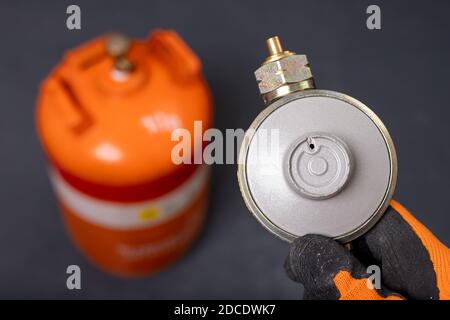 Propane-butane gas cylinder and reducer. Combustible gas used in households. Dark background. Stock Photo