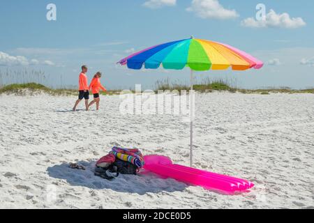 isolated colourful rainbow sun parasol shade with man and woman couple in dayglo shirts at beach at Biloxi Mississippi USA Stock Photo