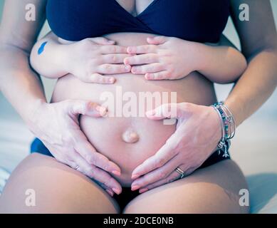 Close up picture of pregnant woman and her baby holding her belly - Baby holding the belly of his pregnant mother - Pregnant woman and her baby holdin Stock Photo