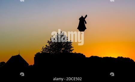 On a hot July evening in the Eastern Netherlands an air balloon shaped like a traditional Dutch windmill is flying across the sky Stock Photo