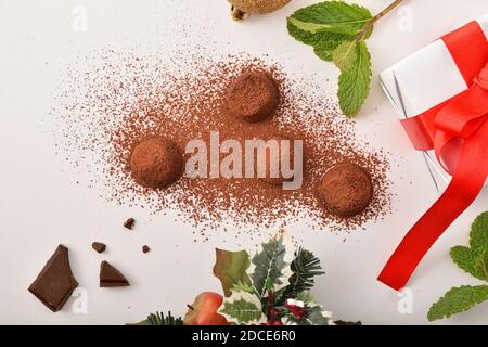 Christmas composition with chocolate truffles sprinkled with cocoa powder on white table with gift and Christmas decoration. Top view. Horizontal comp Stock Photo