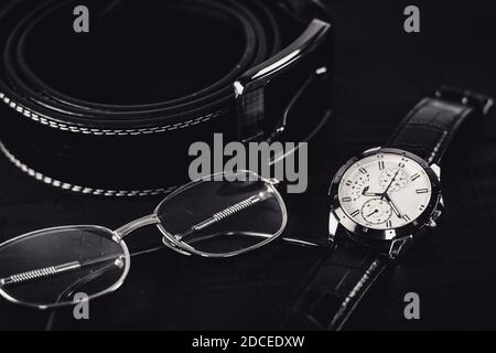 Leather belt, wristwatch and glasses on the wooden table. Close up, black background, male accessories. Stock Photo