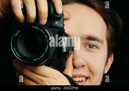 Smiling man takes pictures on Canon camera and tries to focus the lens and takes pictures. Photo editor, cameraman, journalist. Bishkek, Kyrgyzstan - December 15, 2019. Stock Photo