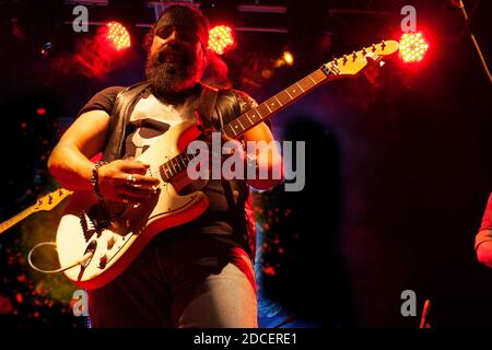 bearded man with bandana tied to his head playing guitar strings exploring musical nightlife in Mexico city illuminated with red light Stock Photo