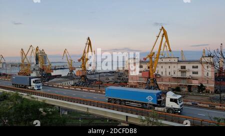 Port cargo terminals and elevated road with cargo vehicle traffic of trailers carrying blue containers. Industrial port landscape in harbor of Europea Stock Photo
