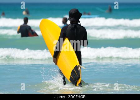 surfer or unidentifiable man in a wetsuit holding a yellow surfboard in the waves at Muizenberg beach, South Africa concept Summer fun on holiday Stock Photo