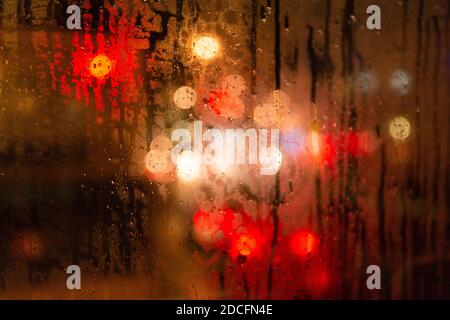 City lights blurred with bokeh effect on a rainy day at night behind raindrop on a windshield Stock Photo
