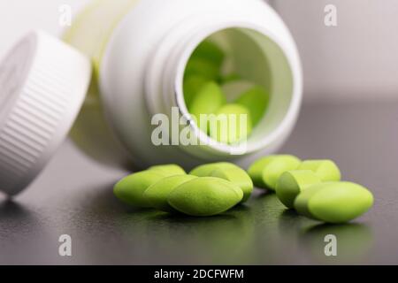 Medical green pills spilling out of a plastic bottle on table top Stock Photo