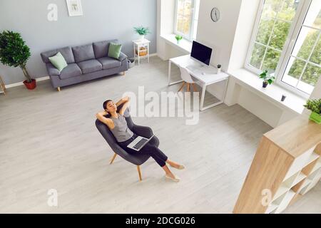 Spacious living room, study or office workspace with woman taking break from work on laptop. Modern interior of new apartment with large windows and p Stock Photo