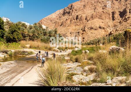 Wadi Tiwi, Oman - February 15, 2020: Tourists visiting Wadi Tiwi oasis with water springs, rocks stone and palm trees, Sultanate of Oman Stock Photo