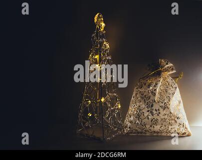 Christmas tree from transparent plastic with illumination and empty gift pouch in golden colors at dark cozy background Stock Photo