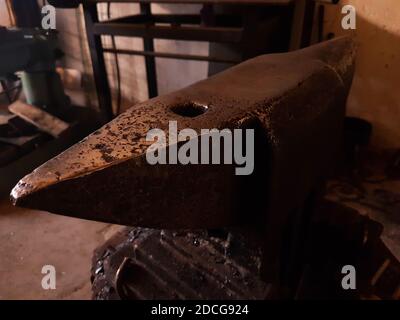 Heavy old vintage hammer placed on durable rusty steel anvil in dark smithery Stock Photo