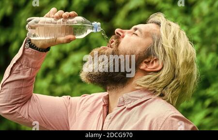 Water balance. Man bearded tourist drinking water plastic bottle nature background. Thirsty guy drinking bottled water. Healthy lifestyle. Safety and health. Summer heat. Drinking clear water. Stock Photo