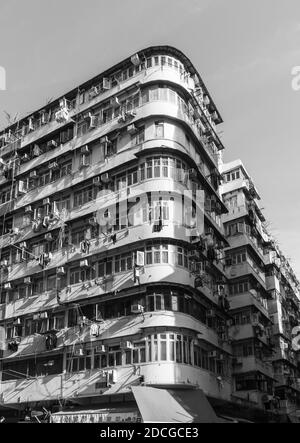 Curved historic corner apartment building in Hong Kong.  Washing and air conditioning units cover the outside.  In black and white. Stock Photo