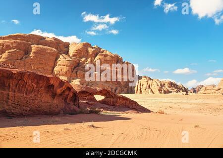 Rocky massifs on red sand desert, small stone arc bridge, bright blue sky in background - typical scenery in Wadi Rum, Jordan Stock Photo