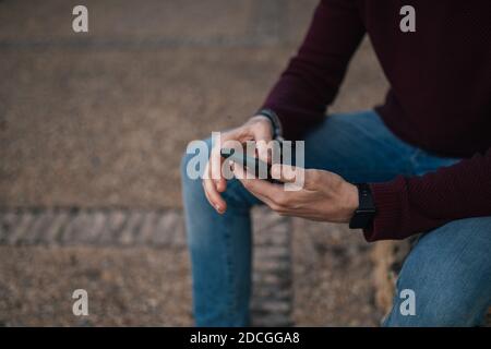 A young boy's hands using his mobile phone on the street in a red T-shirt. Stock Photo