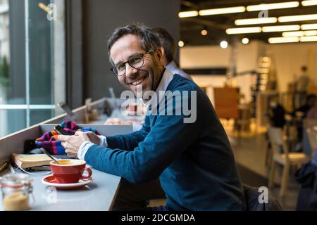 England / London / Young good-looking guy with blue shirt, dark hair and beard is reading and replying to messages and posts online on phone. Stock Photo