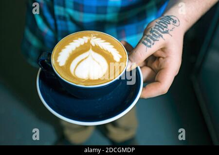 GREAT BRITAIN / England / London/Hand with tatoo holding coffee cup in an indoor cafe in London.Close up of hands holding cup of coffee.