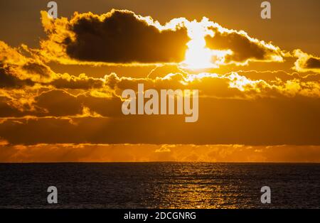 Sunset at sea. Landscape view of the low sun going down over the ocean with cloudy sky, in the UK.