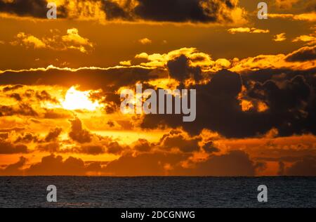 Sunset at sea. Landscape view of the low sun going down over the ocean with cloudy sky, in the UK. Stock Photo