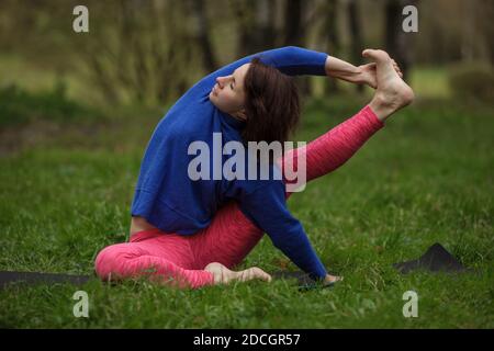 Yoga asanas in nature. Practicing young woman doing kraunchasana at park. Stock Photo