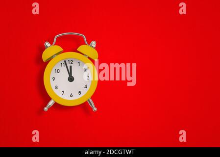 Yellow alarm clock on red paper with copy space. The hands of the clock show twelve o'clock. Stock Photo