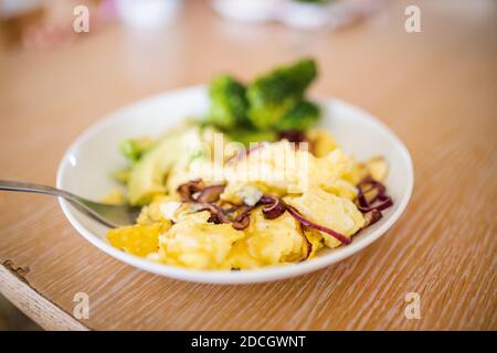 Broccoli and scrambled eggs with avocado slices on wooden table Stock Photo