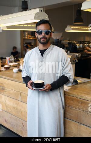 Germany / Berlin /Coffee Style / Young attractive muslim male in traditional Islamic cloting holding cup of coffee at the Barn in Berlin. Stock Photo