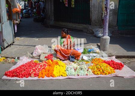 Kolkata, India - March, 2014: Indian woman threading colorful flower garlands and selling for making puja (offering flowers to gods in temple) Stock Photo