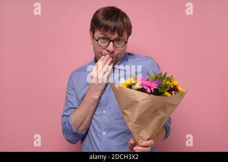 Young funny smiling man holding a bouquet of flowers making a proposal. Stock Photo