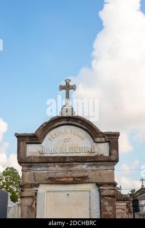 An old, rustic family tomb with a cross on top in a cemetery under a clear blue sky with a few clouds. lafayette cemetery New Orleans Louisiana Stock Photo