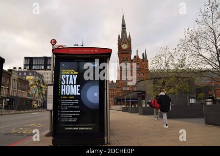 People walk past a Stay Home sign on a bus stop in King's Cross during the second national lockdown in England. London, United Kingdom 21 November 2020. Stock Photo
