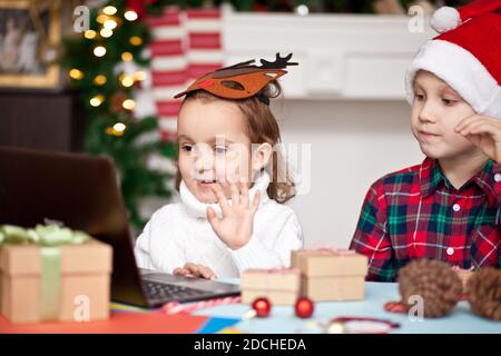 funny kids girl and boy in Santa's cap using a digital tablet laptop notebook. Online call friends or parents and have fun. Stock Photo