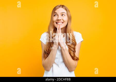 Young focused girl asks God to help her, holding hands near her face, wishes good luck, on a yellow background Stock Photo