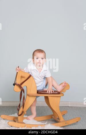 Child Sitting On Ride On Toy In Playroom. Toddler Baby Boy Riding Swinging On Rocking Chair Toy Horse Stock Photo