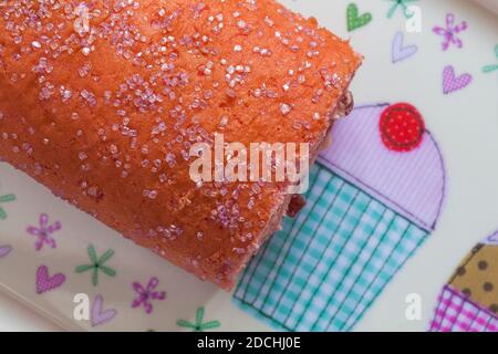 M&S Percy Pig sponge roll cake on plate - pink sponge roll filled with Percy Pig flavour buttercream and fluffy jelly pieces Stock Photo