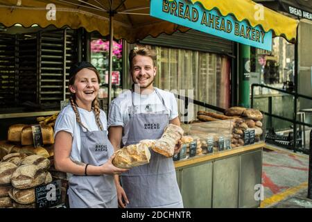 Happy female and male vendor at the Bread Ahead stall at Borough Market, Southwark, South London, Stock Photo