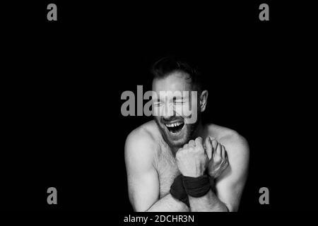 A man with his hands tied on a dark background laughs. Mental illness Stock Photo