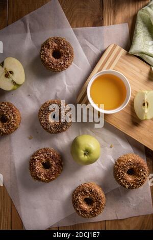 Baked apple cider donuts with apples, cider and textile napkin on baking sheets on natural wooden table. Ready to eat snack. Small batch of homemade f Stock Photo