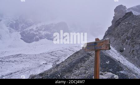 Wooden sign with arrow marking the hiking trail over glacier 'Suldenferner' in snow-covered Ortler mountain massif near Sulden, South Tyrol, Italy. Stock Photo