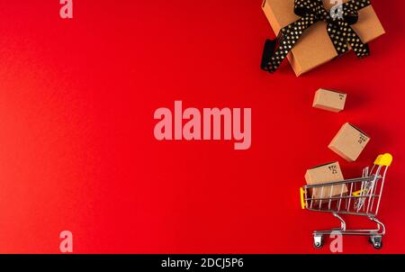 Top view of toy shopping cart with boxes and gift on red background. Copy space for text or design. Sale, discount, shopping and delivery concept. Con Stock Photo