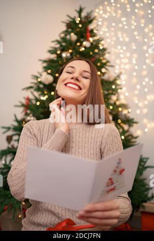 Beautiful woman laughing while reading a Christmas greeting card with light in background. Copy space for text. Stock Photo