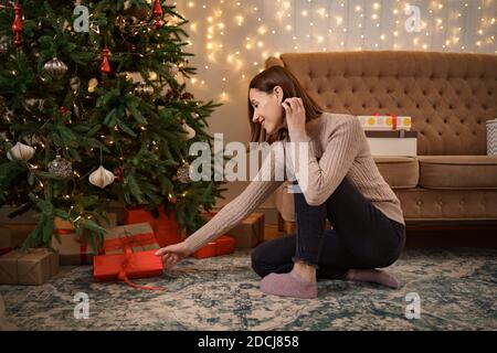 winter holidays, celebration and people concept - close up of woman putting present under christmas tree Stock Photo