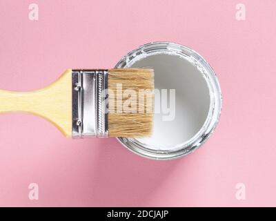 Close-up of new natural bristle brush with wooden handle on an open white paint can over pastel pink textured background. Construction painting work. Stock Photo